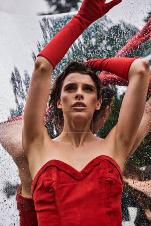 An elegant woman in a flowing red dress and long gloves, embracing the summer breeze in a natural setting.