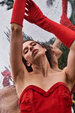 Une jeune femme gracieuse dans une robe rouge vibrante et de longs gants se tient paisiblement, embrassant la brise d'été dans la nature.