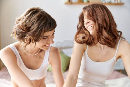 Foto de Dos jóvenes vestidas con ropa cómoda comparten un momento de risa en una cama. - Imagen libre de derechos