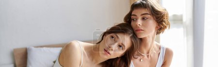 Photo for Two women in comfortable attire sit on a bed, making eye contact with the camera. - Royalty Free Image