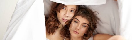 Two women, a loving lesbian couple, cuddle under a cozy blanket in bed.