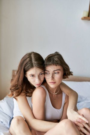 Foto de Una pareja lesbiana con un atuendo acogedor disfrutando de un momento tranquilo sentada en una cama. - Imagen libre de derechos
