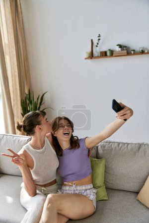 A beautiful lesbian couple relaxes on a couch, one holding a remote control.