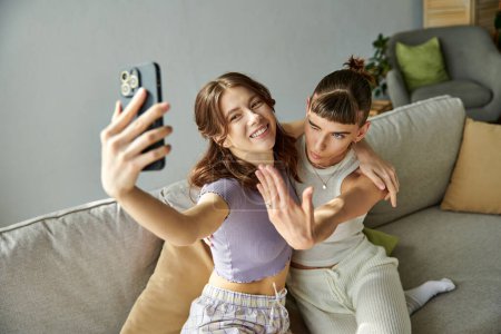 Photo for Two women in comfy attires smiling while taking a selfie on a couch. - Royalty Free Image