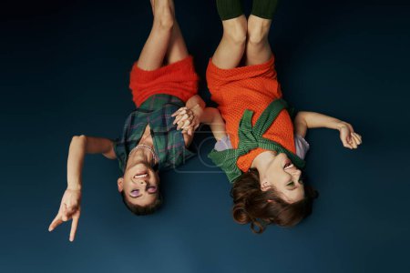 Dos lesbianas tumbadas en el suelo con las manos levantadas en celebración.