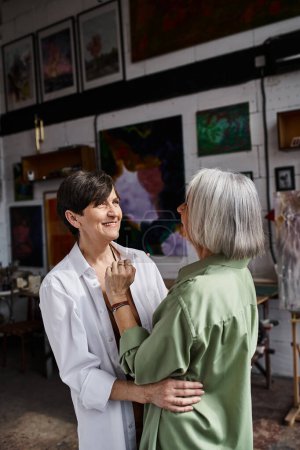 A woman hugs another woman in an art studio.