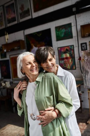 A mature lesbian couple hugging lovingly in studio.