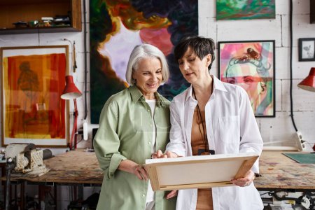 Dos mujeres maduras de pie, colaborando en un estudio de arte lleno de inspiración.