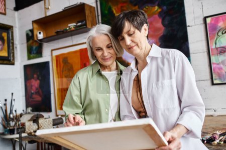 Foto de Una pareja de lesbianas maduras admiran las obras de arte juntas en un estudio. - Imagen libre de derechos