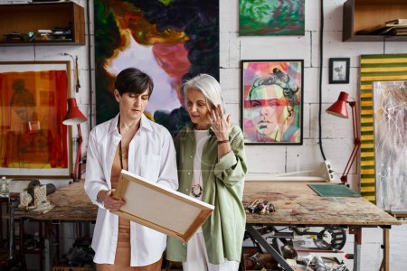 A mature lesbian couple examining painting in studio.