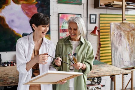Two mature women standing together in an art studio.