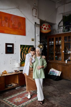Photo for Two mature women stand in a room with a painting on the wall. - Royalty Free Image