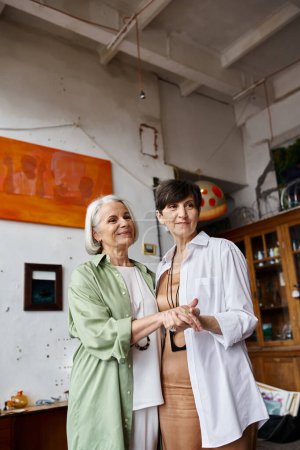 Deux femmes mûres, debout dans un studio d'art, dégagent un sentiment de solidarité.