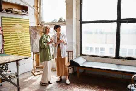 Two mature women sharing a moment of camaraderie in a vibrant art studio.