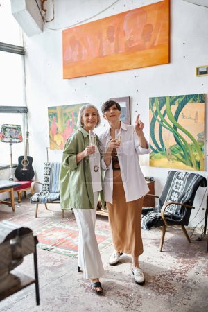 Mature lesbian couple standing in cozy art studio.