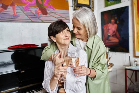 Foto de Two woman share wine in art studio. - Imagen libre de derechos