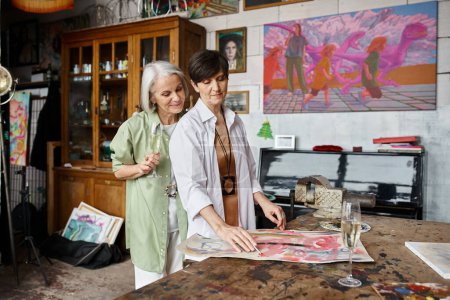 Téléchargez les photos : Mature couple lesbien debout dans un studio d'art, partageant un moment tendre. - en image libre de droit