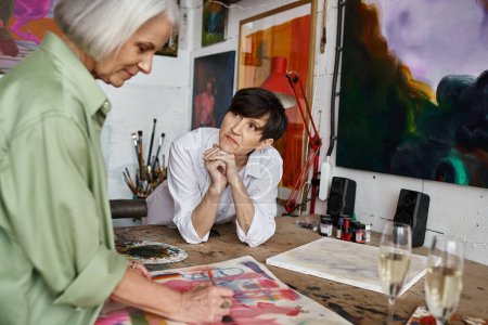 Téléchargez les photos : A woman is seated at a table in front of a captivating painting in an art studio. - en image libre de droit