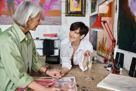 Two woman engage in lively conversation at a table in an art studio.