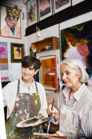 A mature lesbian couple paint in an art studio.