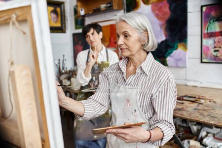 Frau hält Pinsel vor Malerei im Kunstatelier.