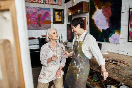 Zwei Frauen, ein reifes lesbisches Paar, tauchen in einem farbenfrohen Atelier in die Kunst ein.