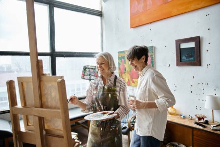 Photo for Two women, mature and in love, stand together in an art studio. - Royalty Free Image