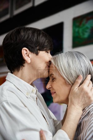 Mature lesbian couple hugging in art studio.