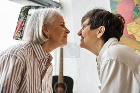 Two women kissing in front of a guitar in art studio.