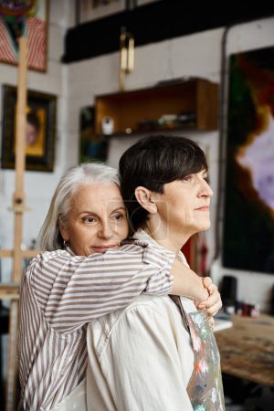 Affectionate moment as mature lesbians hugging in cozy studio.