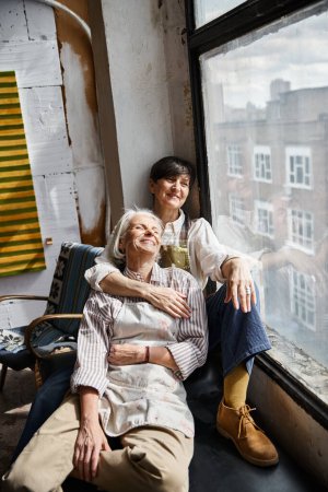 Foto de Dos mujeres se sientan junto a una ventana, compartiendo un momento tranquilo juntas. - Imagen libre de derechos