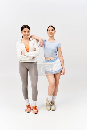 Téléchargez les photos : Brunettes adolescentes, meilleures amies, se tiennent côte à côte dans des vêtements de sport sur fond gris, respirant l'énergie et la camaraderie. - en image libre de droit