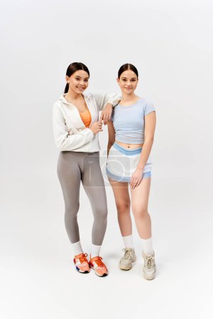 Foto de Dos guapas adolescentes morenas vestidas con ropa deportiva se paran en un estudio, exudando confianza y amistad. - Imagen libre de derechos