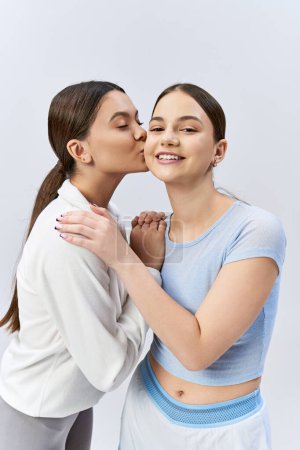 Zwei hübsche Mädchen im Teenageralter, eines im blauen Hemd, küssen sich in einem zarten Moment.