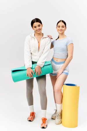 Photo for Two pretty brunette teenage girls in sportive attire standing confidently next to each other in front of a white background. - Royalty Free Image
