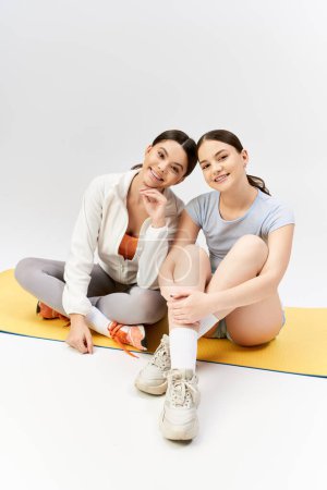 Foto de Dos guapas adolescentes morenas vestidas con ropa deportiva sentadas en una alfombra, posando para la cámara en un estudio. - Imagen libre de derechos