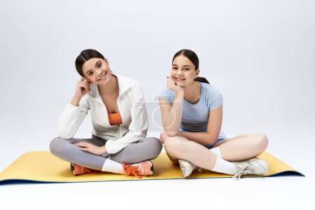 Photo for Two teenage girls, pretty and brunette, sitting on a yoga mat in a studio. They are smiling and posing for a picture. - Royalty Free Image