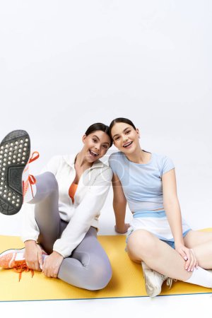 Foto de Dos guapas adolescentes, con el pelo moreno, sentadas en una alfombra con los pies en el suelo en un estudio. - Imagen libre de derechos