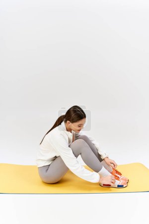 Una guapa adolescente morena en ropa deportiva se sienta con las piernas cruzadas en una alfombra amarilla en un estudio.