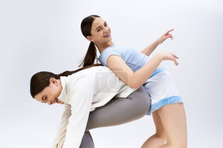 Dos guapas adolescentes morenas con atuendo deportivo muestran sus movimientos de baile en un estudio sobre un fondo gris.