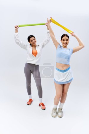 Foto de Dos guapas adolescentes morenas vestidas con ropa deportiva se unen, exudando fuerza y amistad sobre un fondo gris de estudio. - Imagen libre de derechos