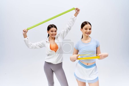 Photo for Two pretty, brunette teenage girls in sportive attire pose, standing side by side as best friends, against a grey studio background. - Royalty Free Image