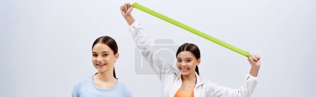Foto de Two pretty, young women with brunette hair stand side by side in sporty outfits against a grey studio backdrop. - Imagen libre de derechos
