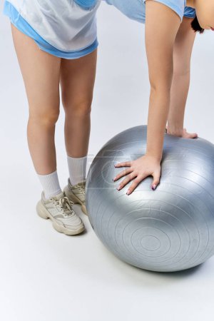 Photo for A pretty, brunette teenage girl in sportive attire gracefully balances on an exercise ball, showing strength and agility. - Royalty Free Image