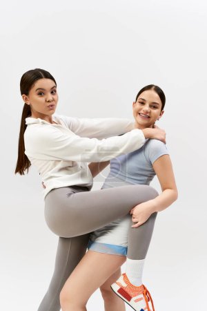 Foto de Dos adolescentes bonitas y deportivas vestidas con atuendo atlético posan juntas en un estudio sobre un fondo gris. - Imagen libre de derechos