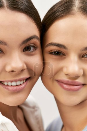Two pretty brunette teenage girls smiling and posing for a picture in a studio against a grey background.