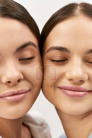 Photo for Two young, brunette women standing confidently side by side in a studio against a grey background. - Royalty Free Image