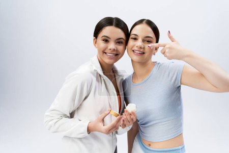Zwei hübsche, brünette Teenager-Mädchen in sportlicher Kleidung lächeln und posieren vor grauem Studiohintergrund für die Kamera.