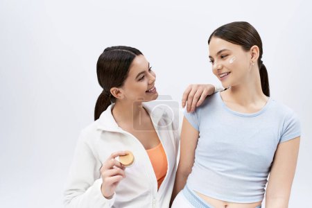 Zwei junge Mädchen, hübsch und brünett, stehen in sportlicher Kleidung zusammen und strahlen vor grauem Hintergrund Zuversicht und Freundschaft aus..