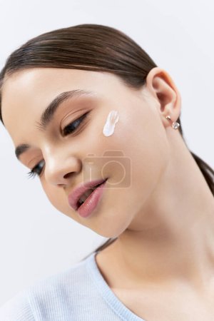 A pretty, brunette teenage girl with cream on her face, feeling pampered and relaxed in a serene studio setting.